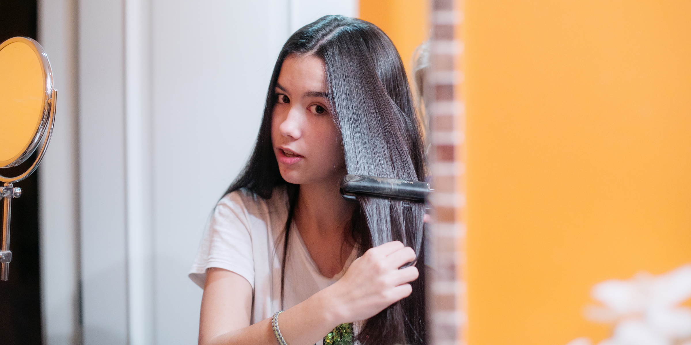 young brunette long haired teenager using hair straightener